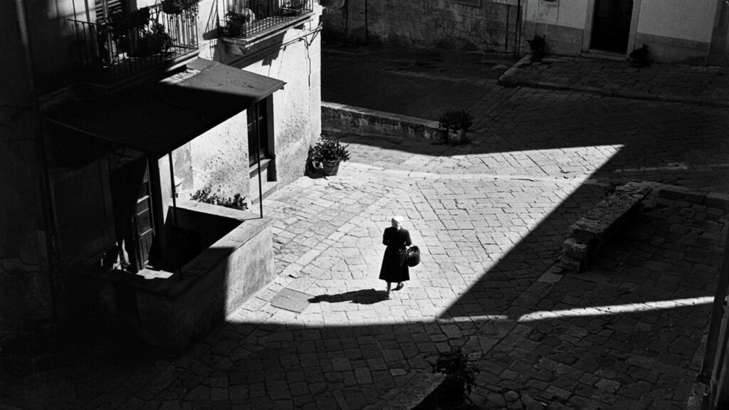 Place méditerranéenne vue d’en haut, une femme traverse un triangle de lumière, illustration générée par IA dans l’esprit de Henri Cartier-Bresson